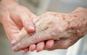 A person holding an elderly hand with one finger.