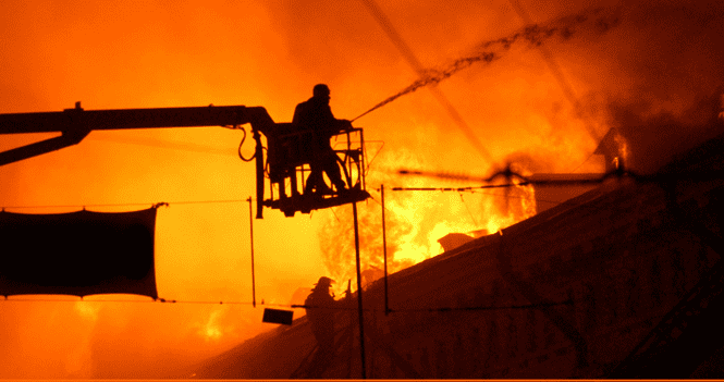 A man on a crane in front of a fire.